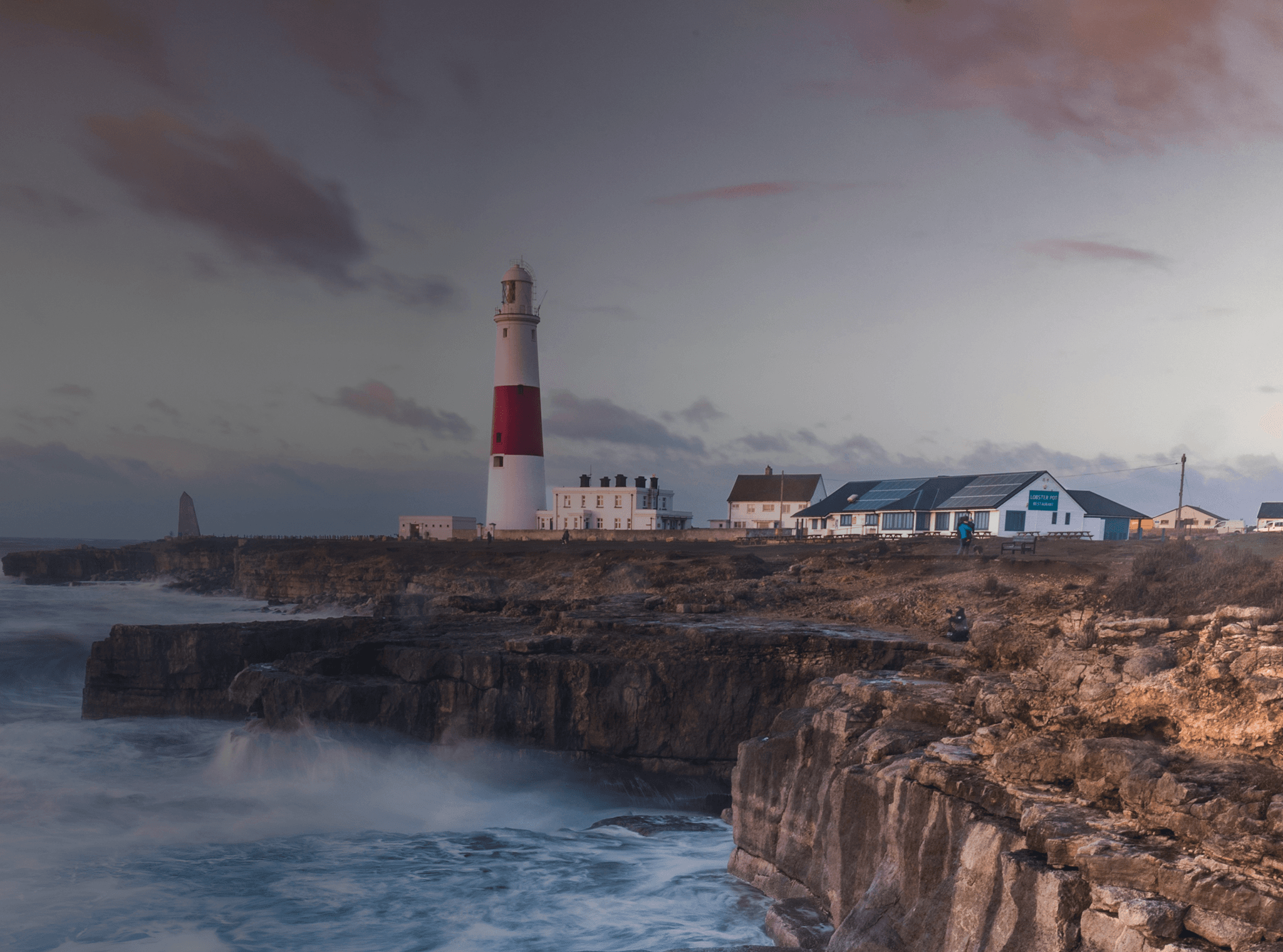 Des vagues s'écrasent sur une falaise britannique avec un phare au loin