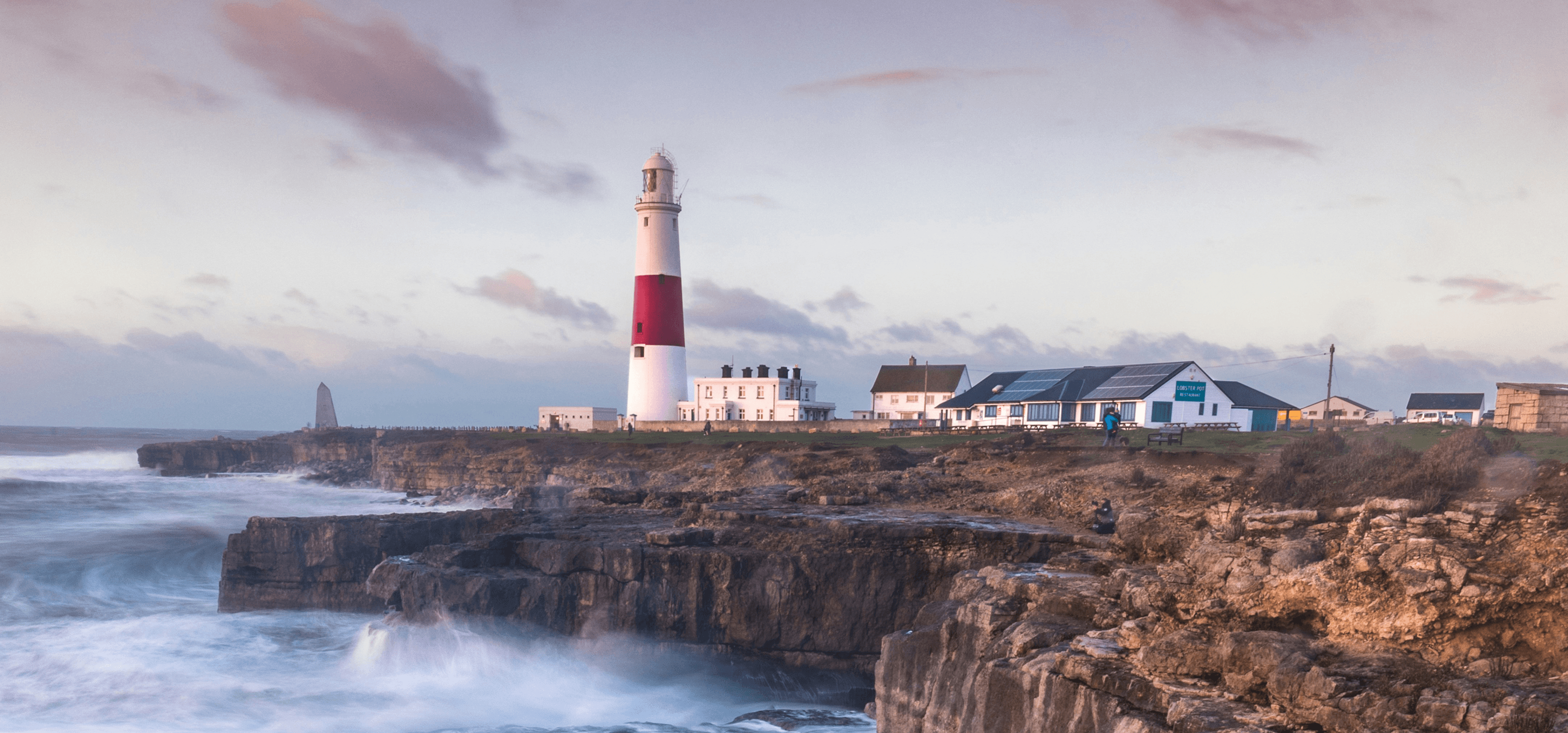 Des vagues s'écrasent sur une falaise britannique avec un phare au loin