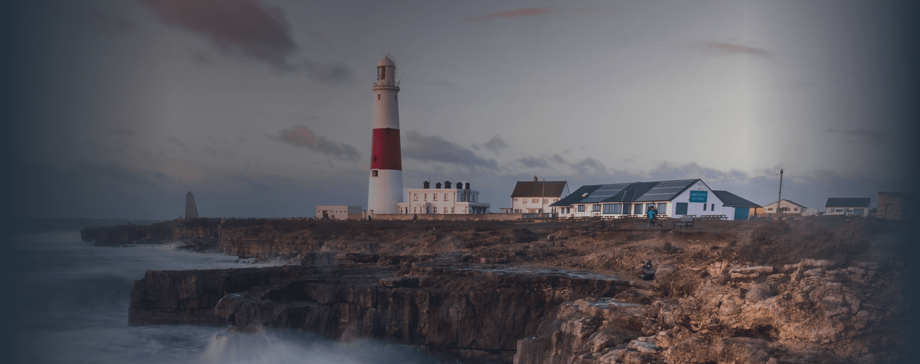 Des vagues s'écrasent sur une falaise britannique avec un phare au loin