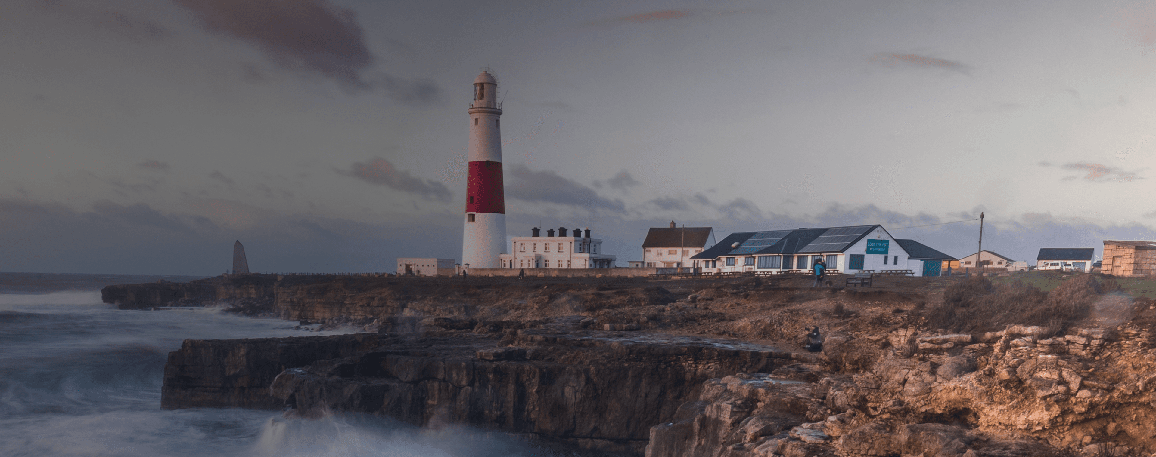 Des vagues s'écrasent sur une falaise britannique avec un phare au loin