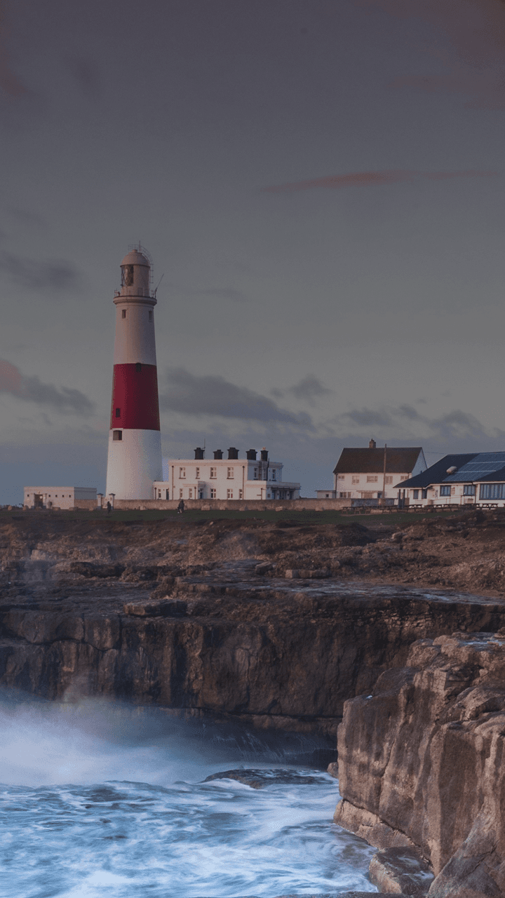 Des vagues s'écrasent sur une falaise britannique avec un phare au loin