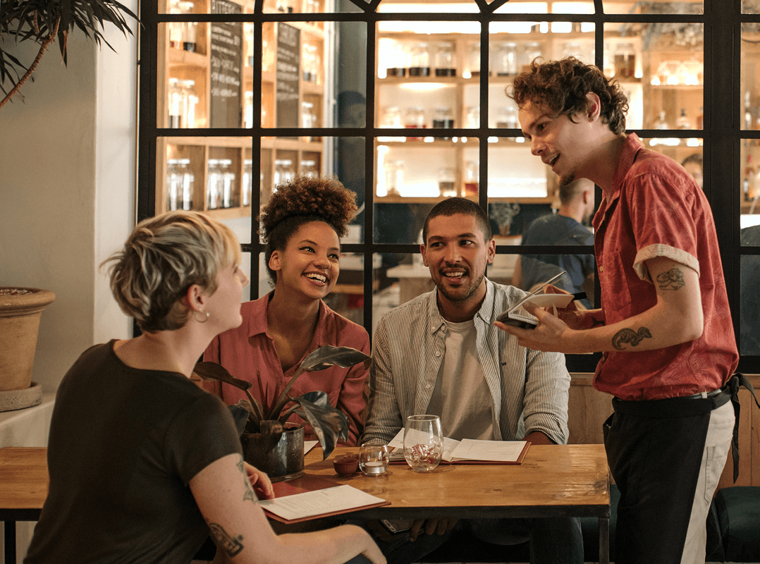Un groupe d'amis pratiquent une nouvelle langue qu'ils ont apprise tout en passant leur commande à un serveur dans un café élégant.