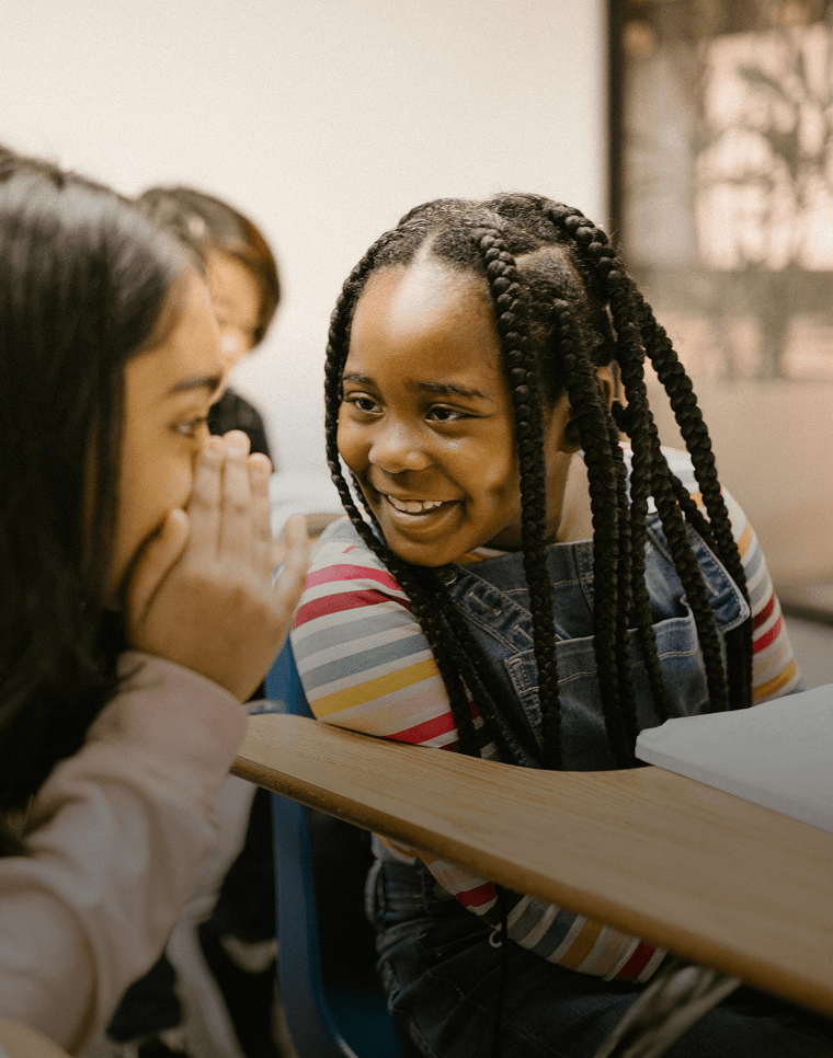 Des élèves souriants chuchotent entre eux pendant qu'ils apprennent une nouvelle langue à l'école.