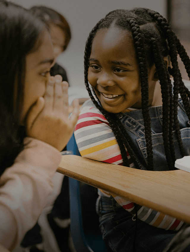 Des élèves souriants chuchotent entre eux pendant qu'ils apprennent une nouvelle langue à l'école.
