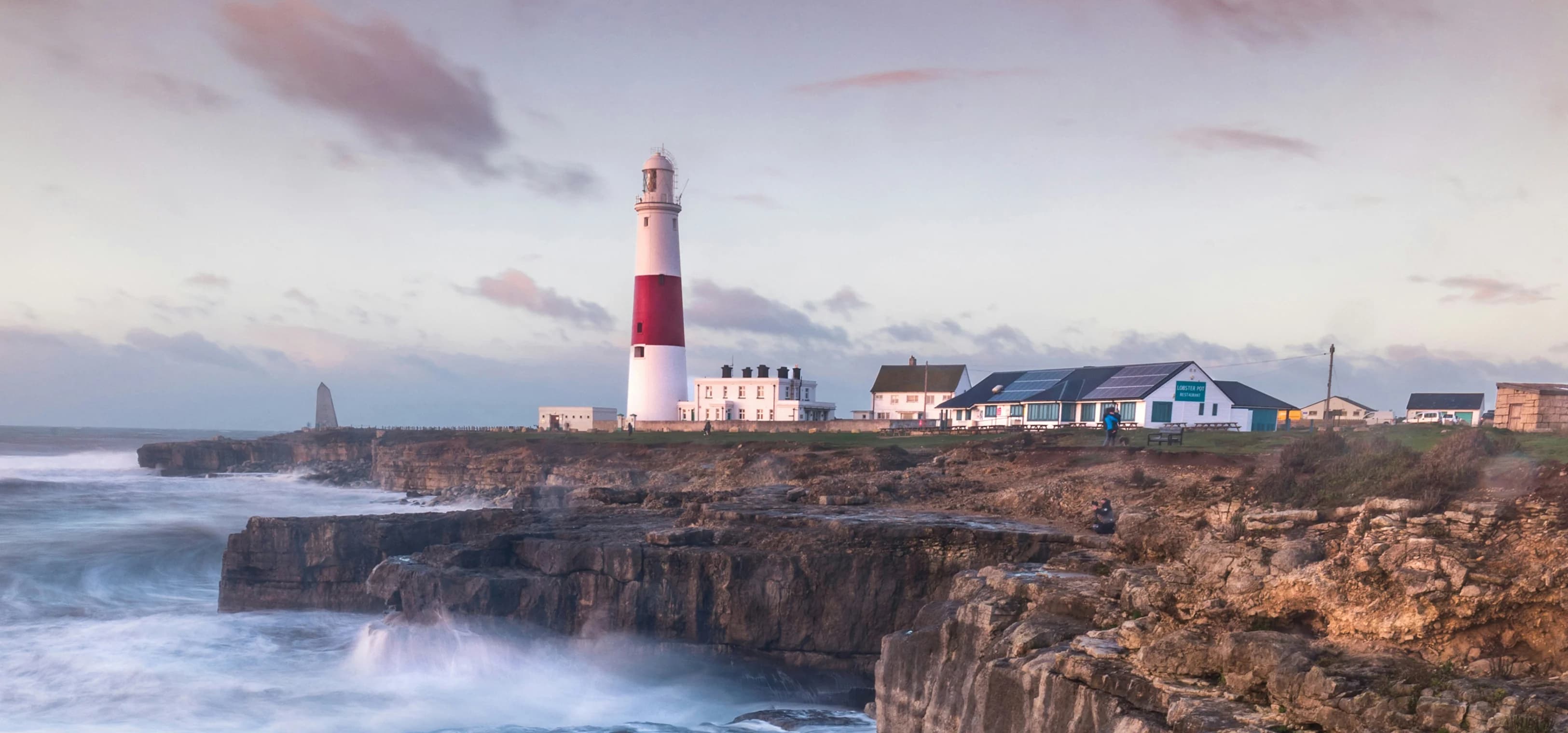 Des vagues s'écrasent sur une falaise britannique avec un phare au loin