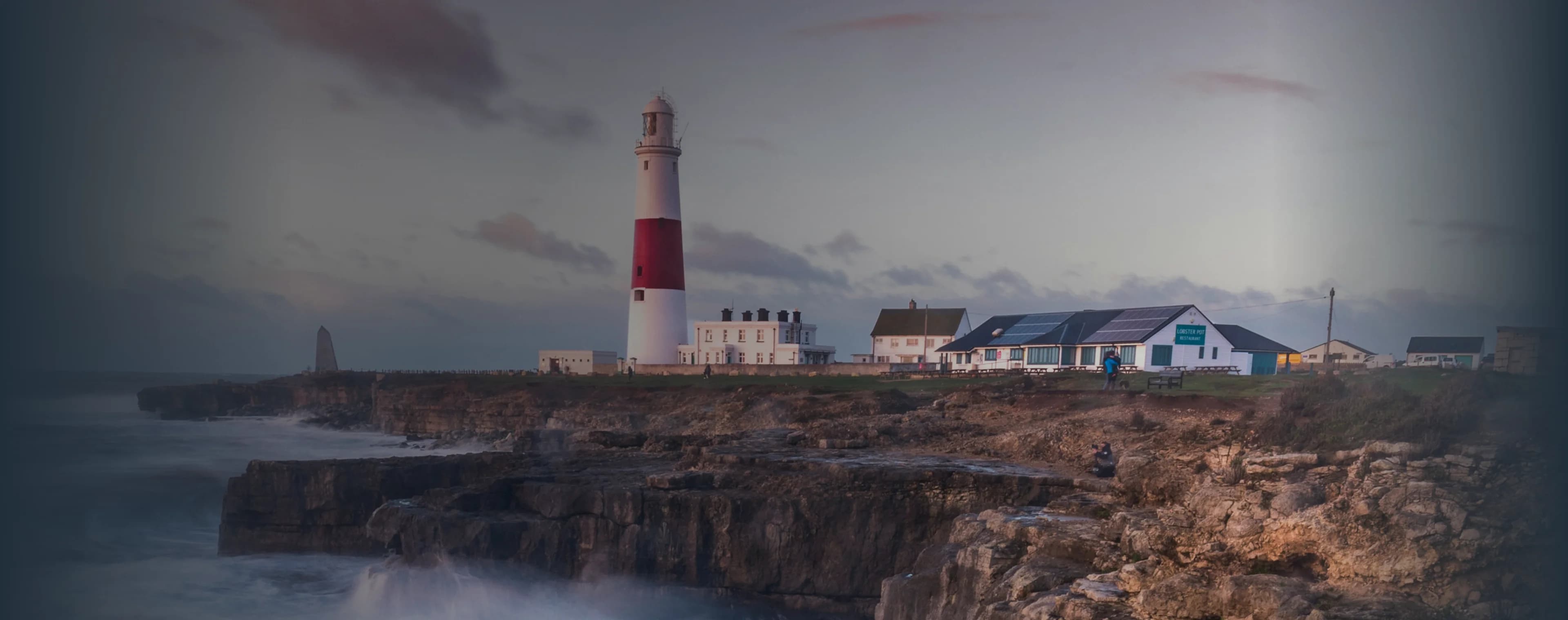 Des vagues s'écrasent sur une falaise britannique avec un phare au loin