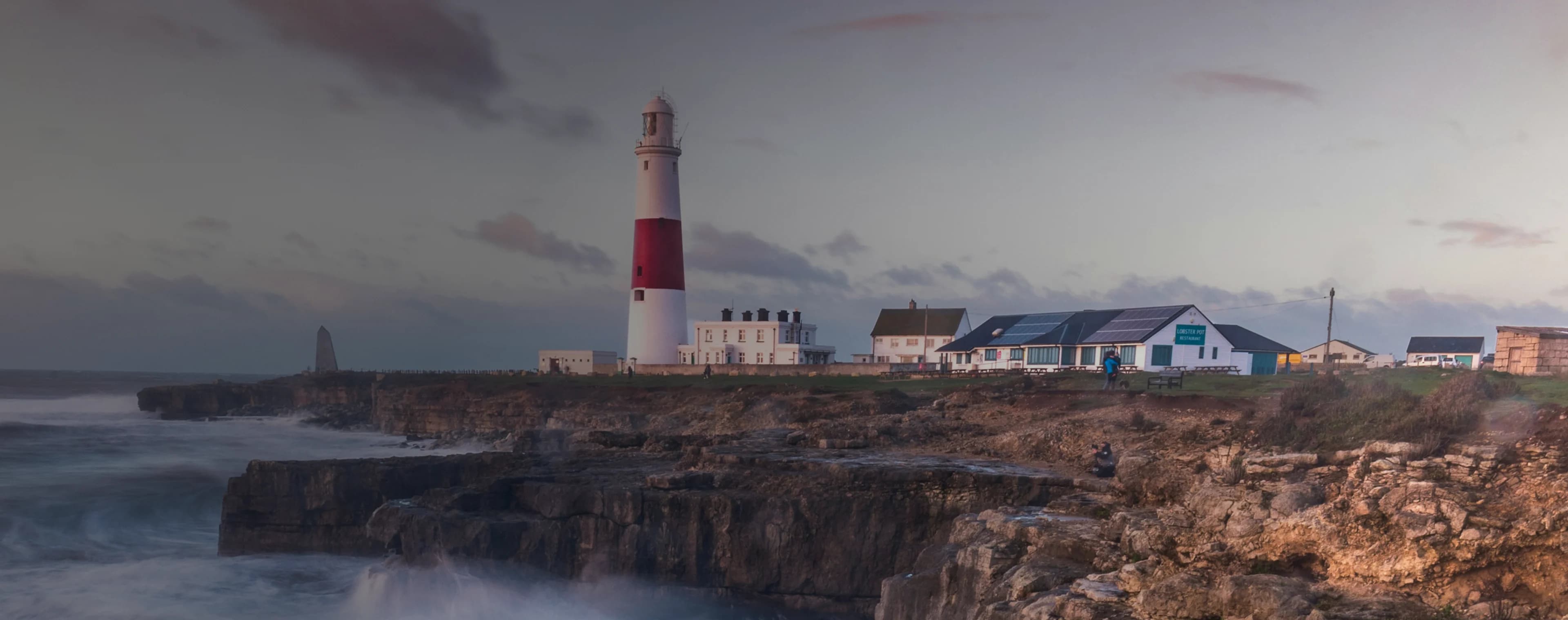 Des vagues s'écrasent sur une falaise britannique avec un phare au loin