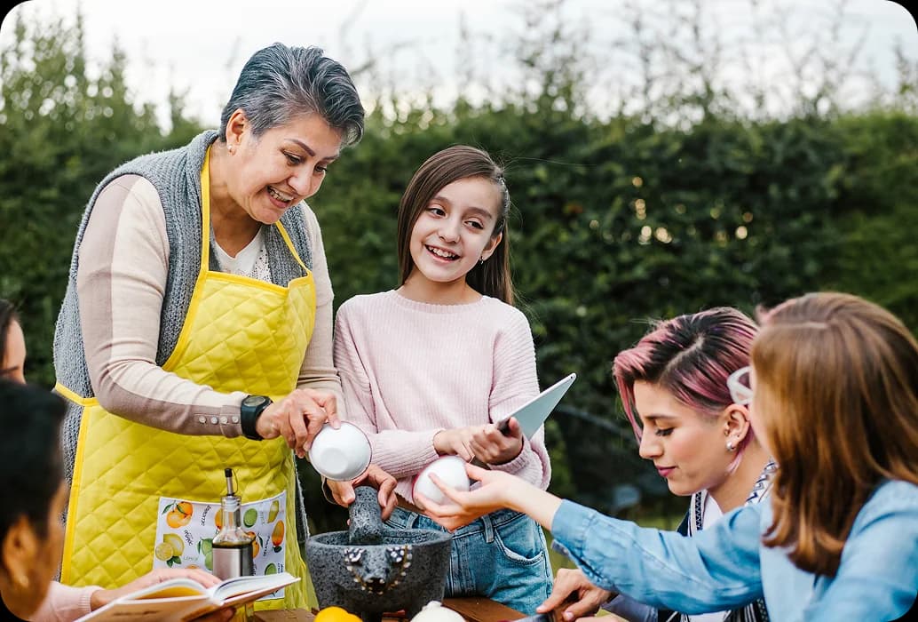 Un adulte apprend à des enfants à préparer des ingrédients à l'aide d'un mortier et d'un pilon lors d'une activité d'apprentissage culturelle en plein air.